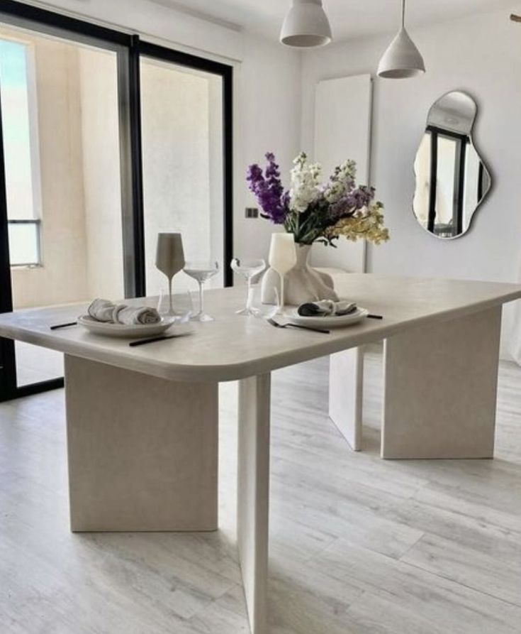 a dining room table and chairs with flowers in vases on the end, next to an open patio door