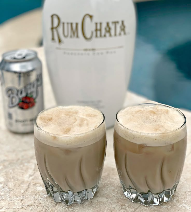 two glasses filled with liquid sitting on top of a table next to a bottle of rumchata