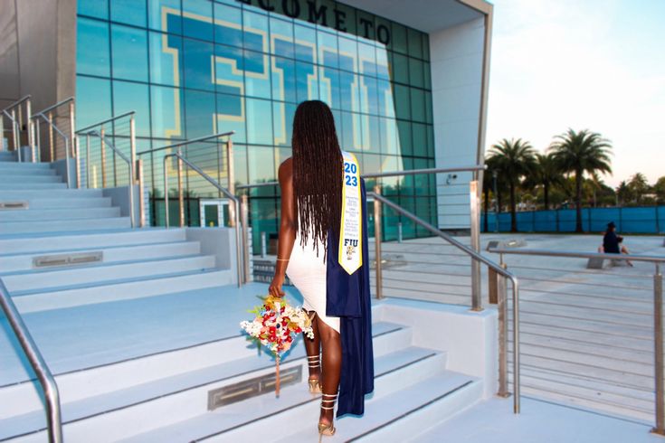 a woman is walking down the stairs with flowers in her hand and a sash around her neck