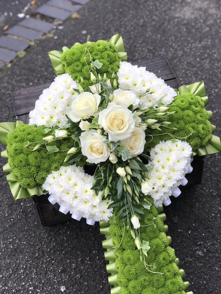 a bouquet of white and green flowers on a wooden cross shaped arrangement in the street