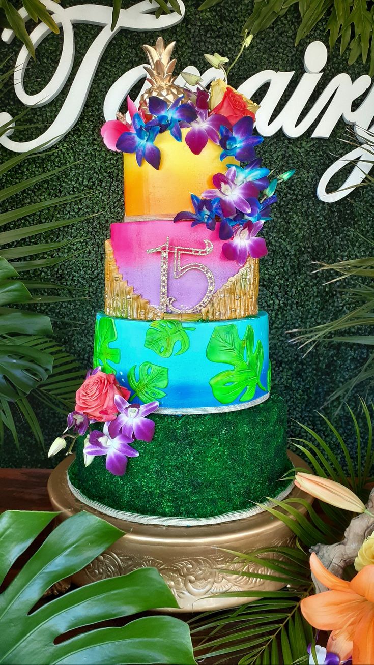 there is a multi layer cake with flowers on the top and green grass around it