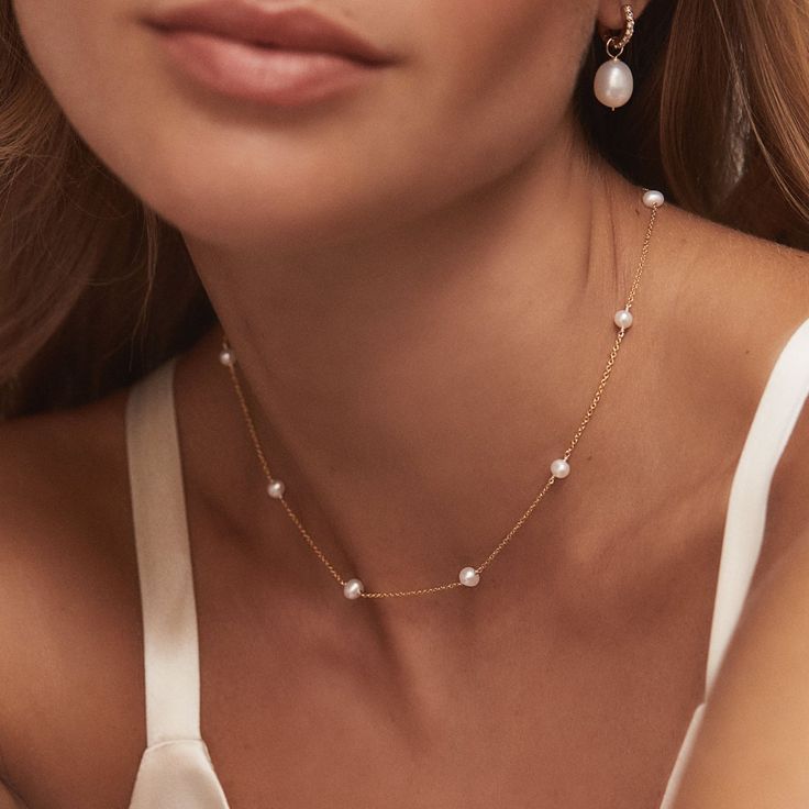 a close up of a woman wearing a necklace with pearls on the bottom and an earring