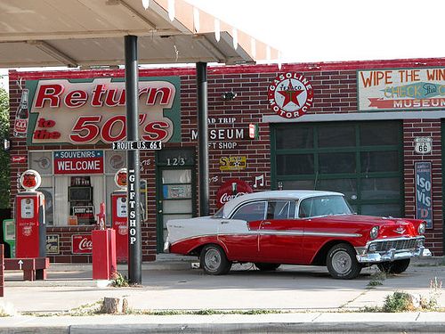 an old red and white car parked in front of a gas station