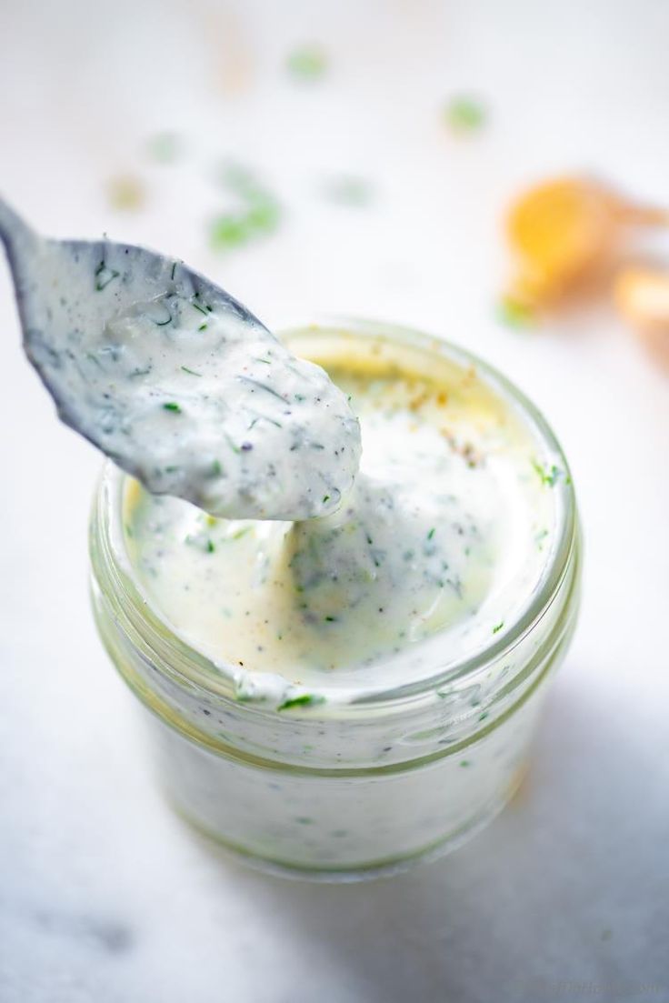 a spoon full of mayonnaise sitting on top of a glass jar filled with dressing