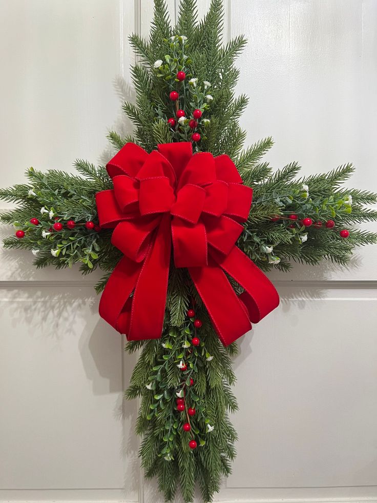 a cross decorated with holly and red bow hanging on the wall next to a door