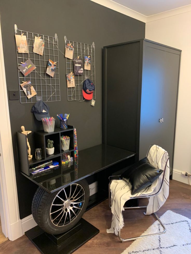 a room with a black desk, chair and shelves on the wall next to it