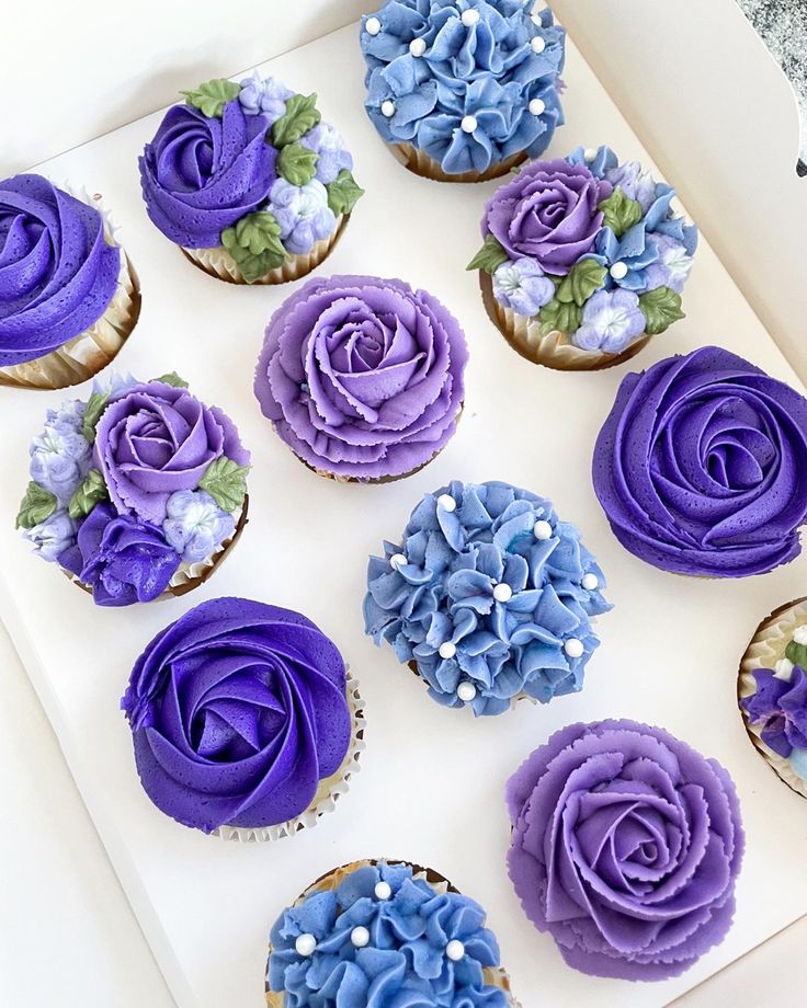 cupcakes with purple and blue frosting in a white box on a table