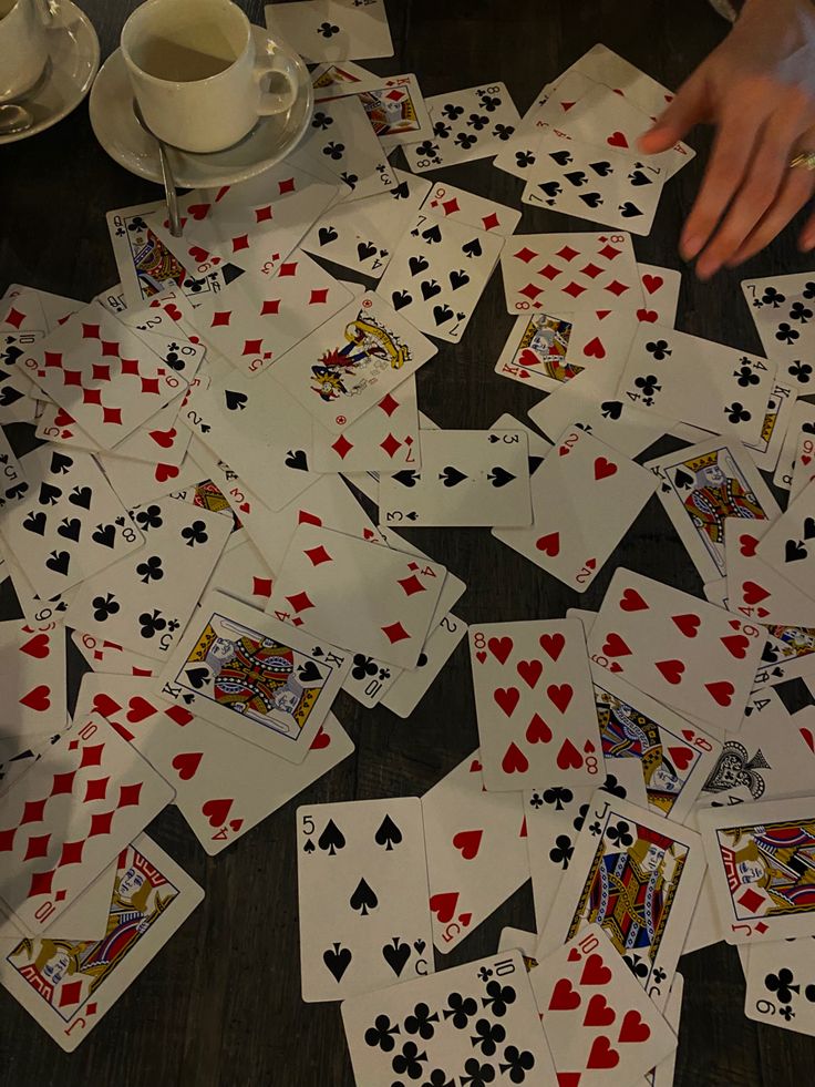 a table topped with lots of playing cards next to a cup of coffee and saucer