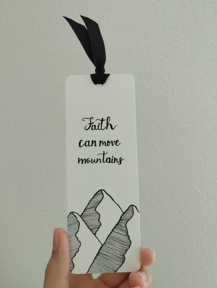 a person holding up a bookmark with the words faith can move mountains on it