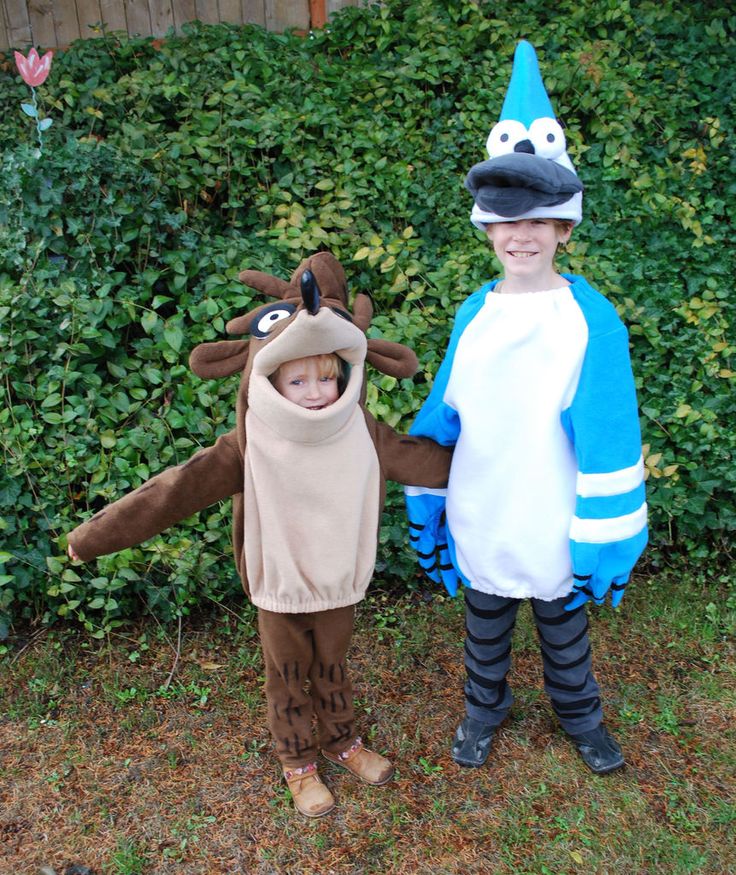 two children dressed up in costumes standing next to each other on the grass near bushes