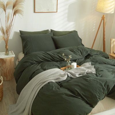 a bed with green sheets and pillows in a white room next to a wooden table