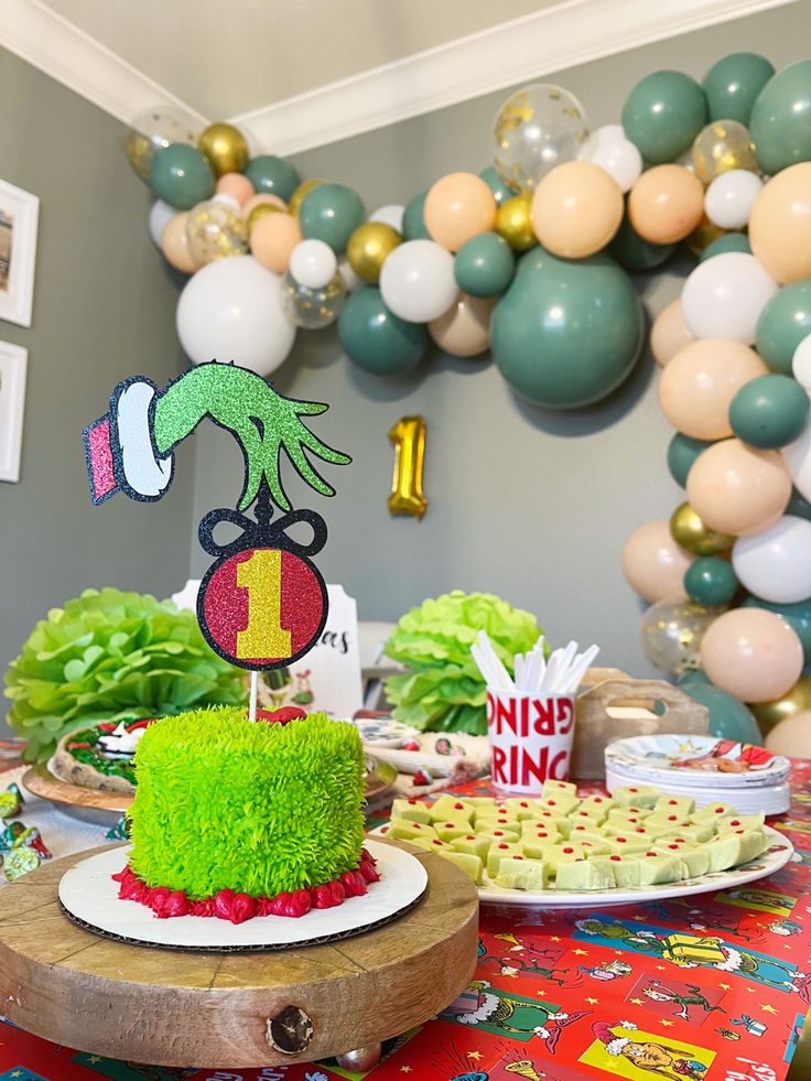 a table topped with cake covered in green frosting next to balloons and other decorations