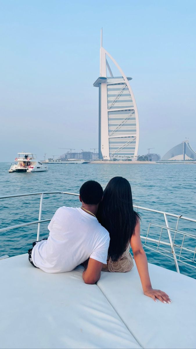 two people are sitting on the back of a boat looking at the burj