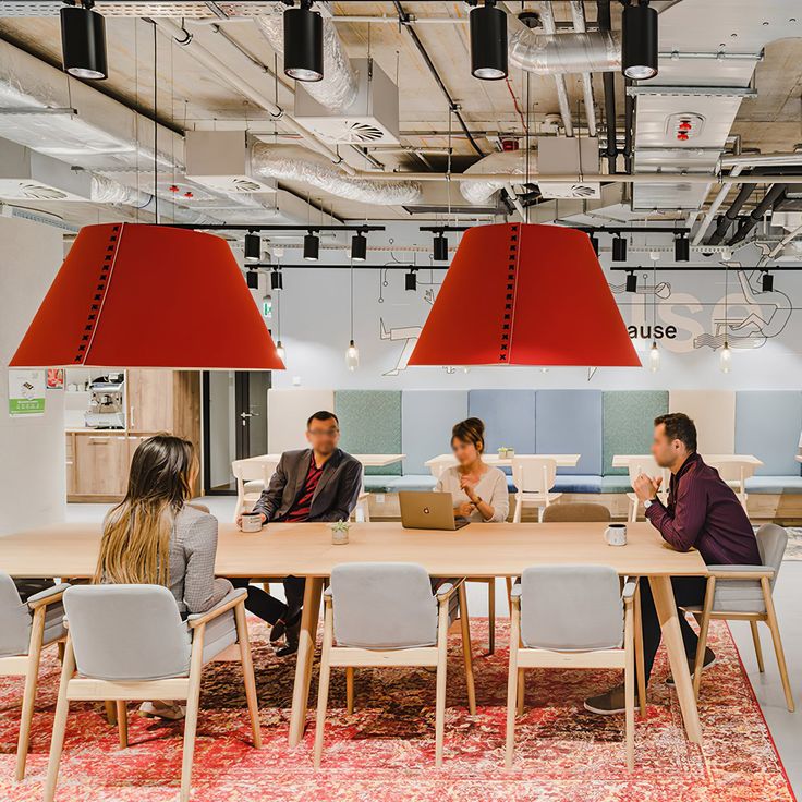 people are sitting at a table in an office with red lamps hanging from the ceiling