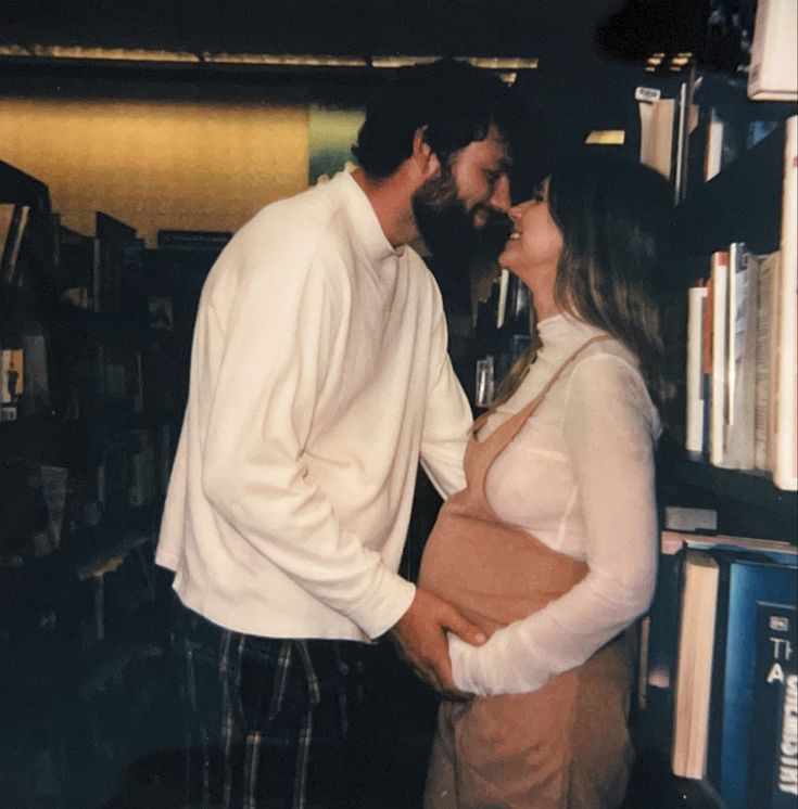 a man and woman standing next to each other in front of a bookshelf