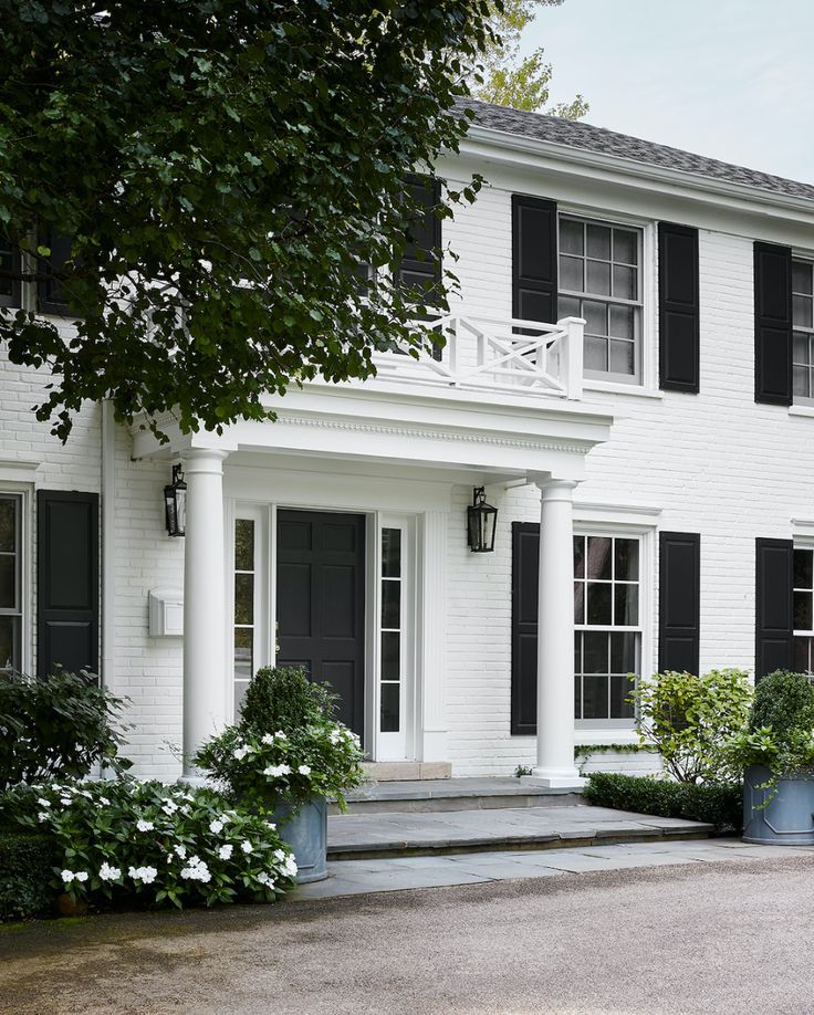 a white house with black shutters on the front door and windows, along with potted plants