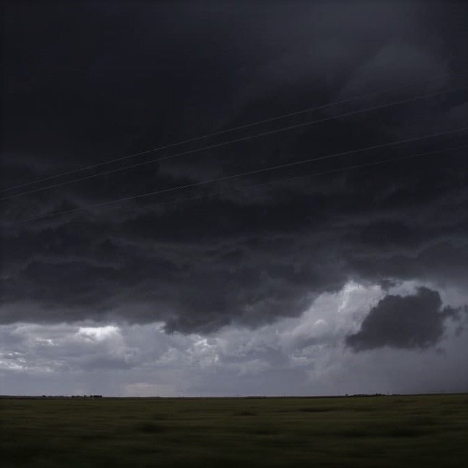 the sky is dark and cloudy over an open field