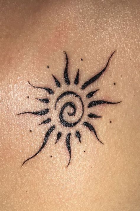 a sun tattoo on the back of a woman's shoulder and chest, it is black