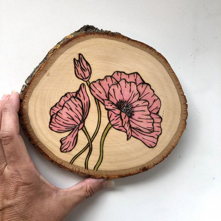 a hand holding a piece of wood with flowers painted on it