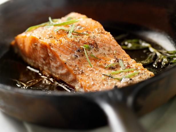 a piece of salmon is being cooked in a skillet with some herbs on top