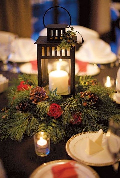 a candle is lit on top of a table decorated with evergreen and red roses, pine cones and greenery