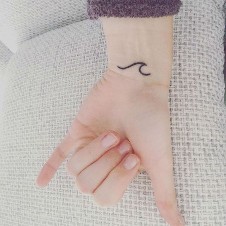 a woman's hand with a small wave tattoo on it