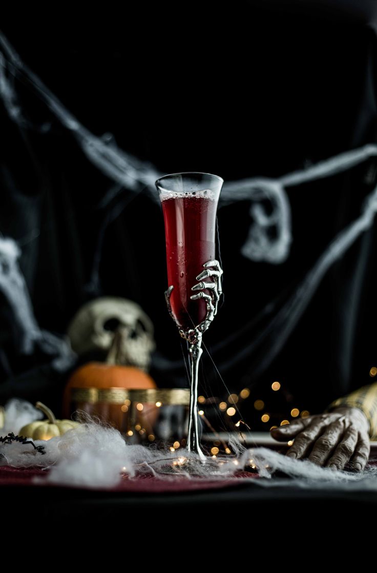 a skeleton holding a wine glass in front of a table with halloween decorations on it