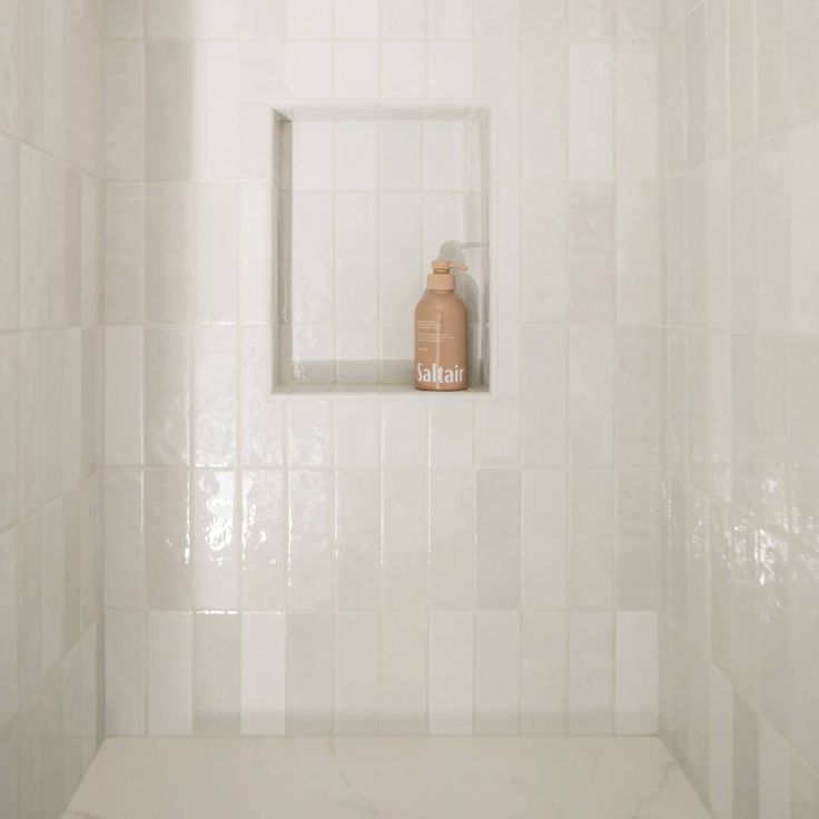 a white tiled shower with a bottle in the corner