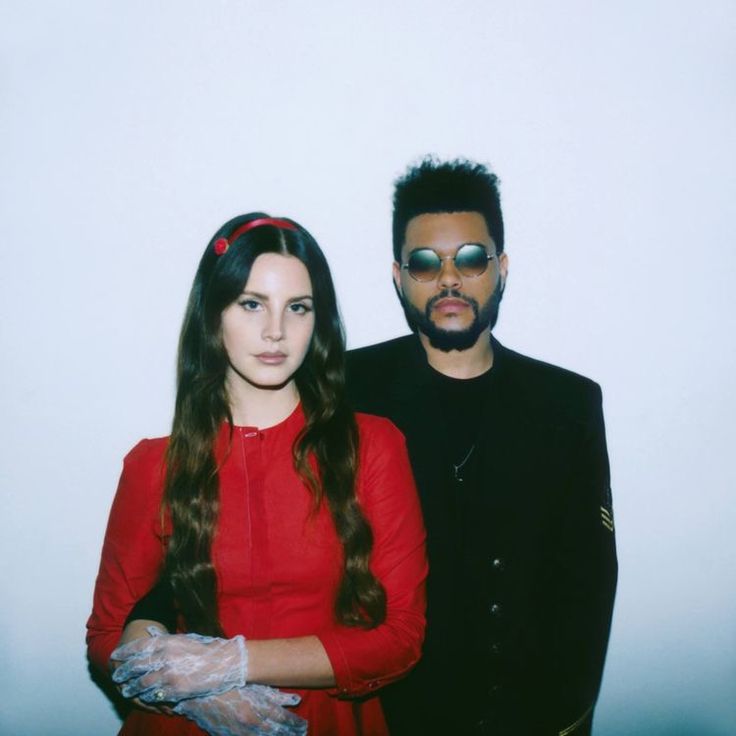 a man and woman standing next to each other in front of a white wall wearing gloves