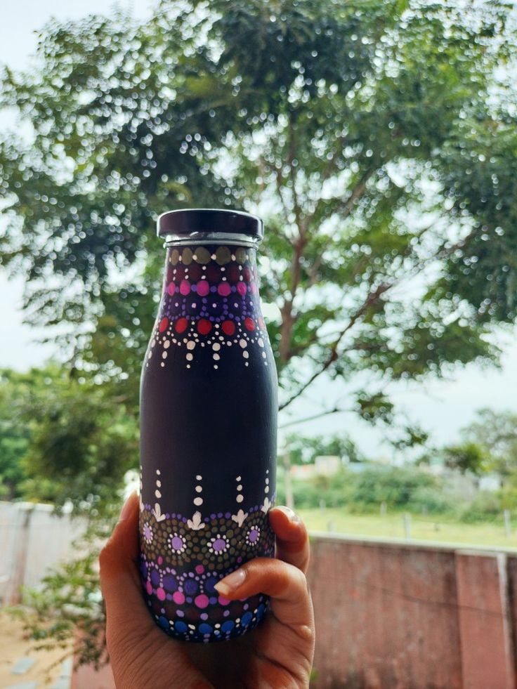 a hand holding a black and purple vase in front of a tree