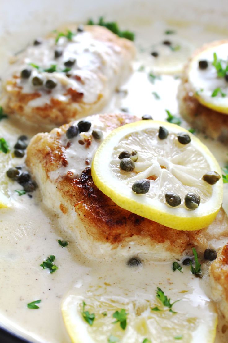 some chicken with lemon slices and capers in a white sauce on top of a pan