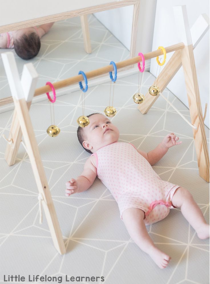 a baby laying on its back in front of a wooden frame with the words, how to plan a baby play at 2 months