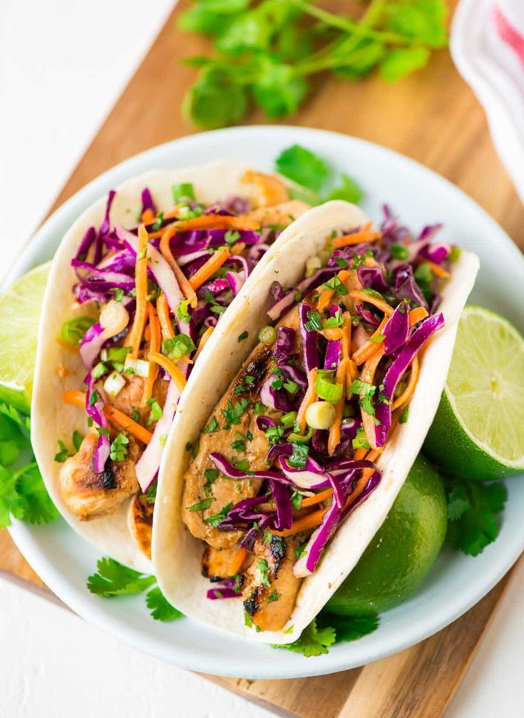 two fish tacos with cole slaw and lime wedges on a white plate