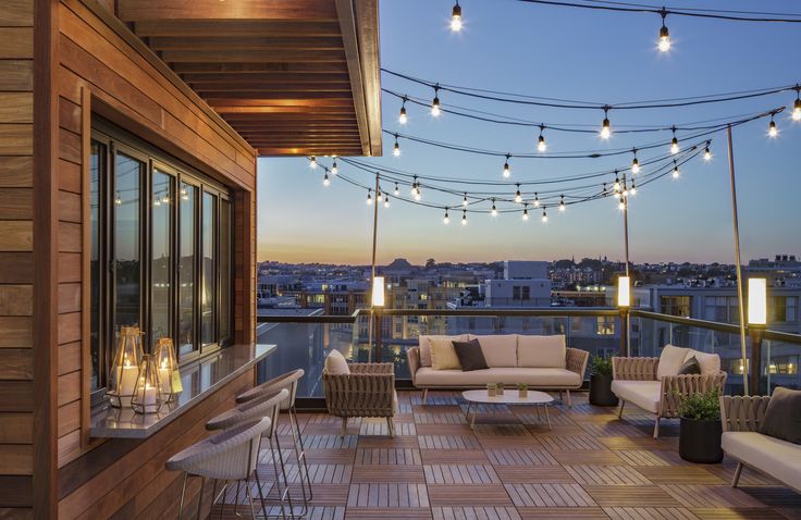 an outdoor patio with string lights and furniture on the balcony overlooking the city at night