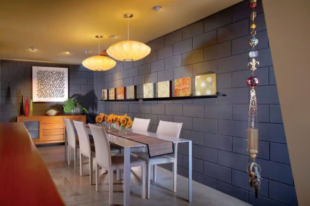 a dining room table with white chairs next to a gray brick wall and orange accents