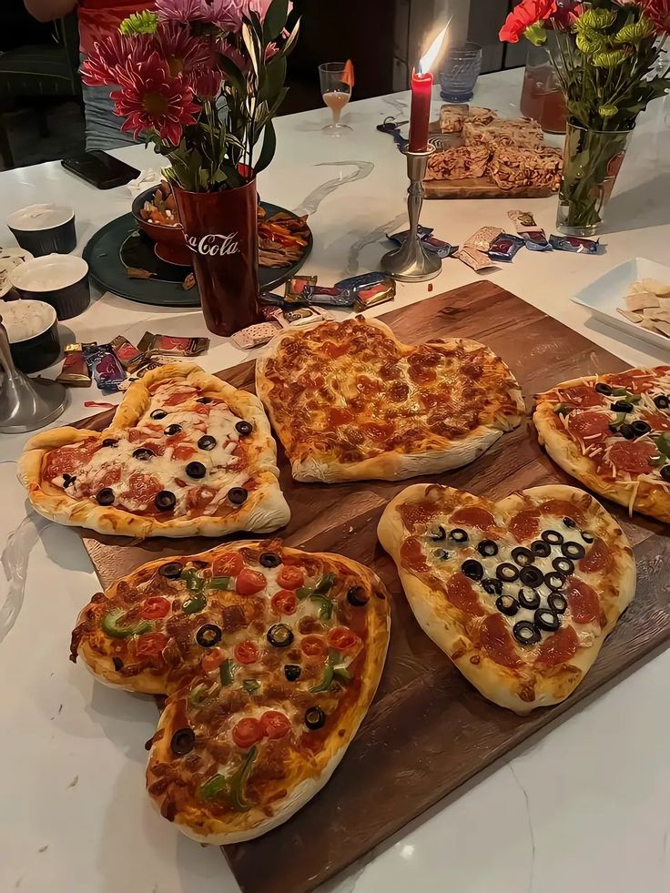 heart shaped pizzas on a wooden cutting board with candles and flowers in the background