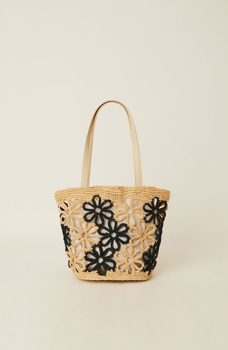 a straw bag with black and white flowers on the front, sitting against a white background