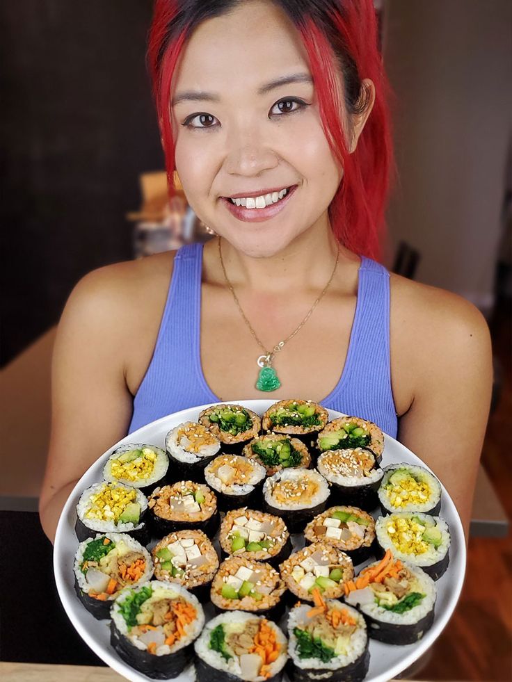 a woman with red hair holding up a plate of sushi and other food items