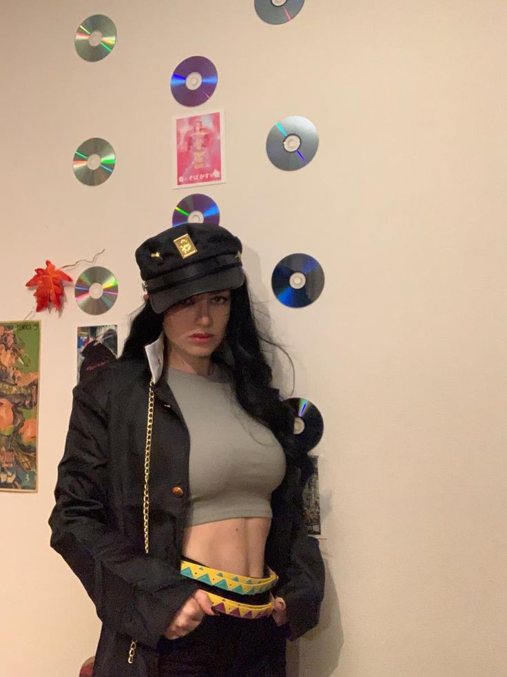 a woman in black jacket and hat standing next to wall with cds on it