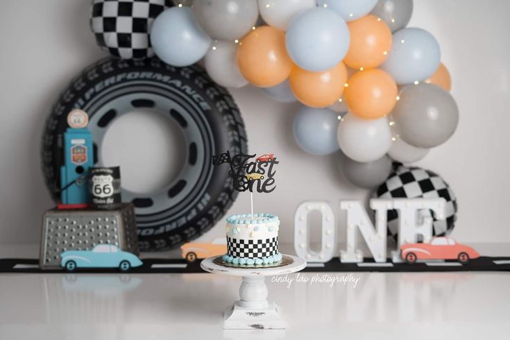 a birthday party with cars and balloons on the wall, including a race car cake