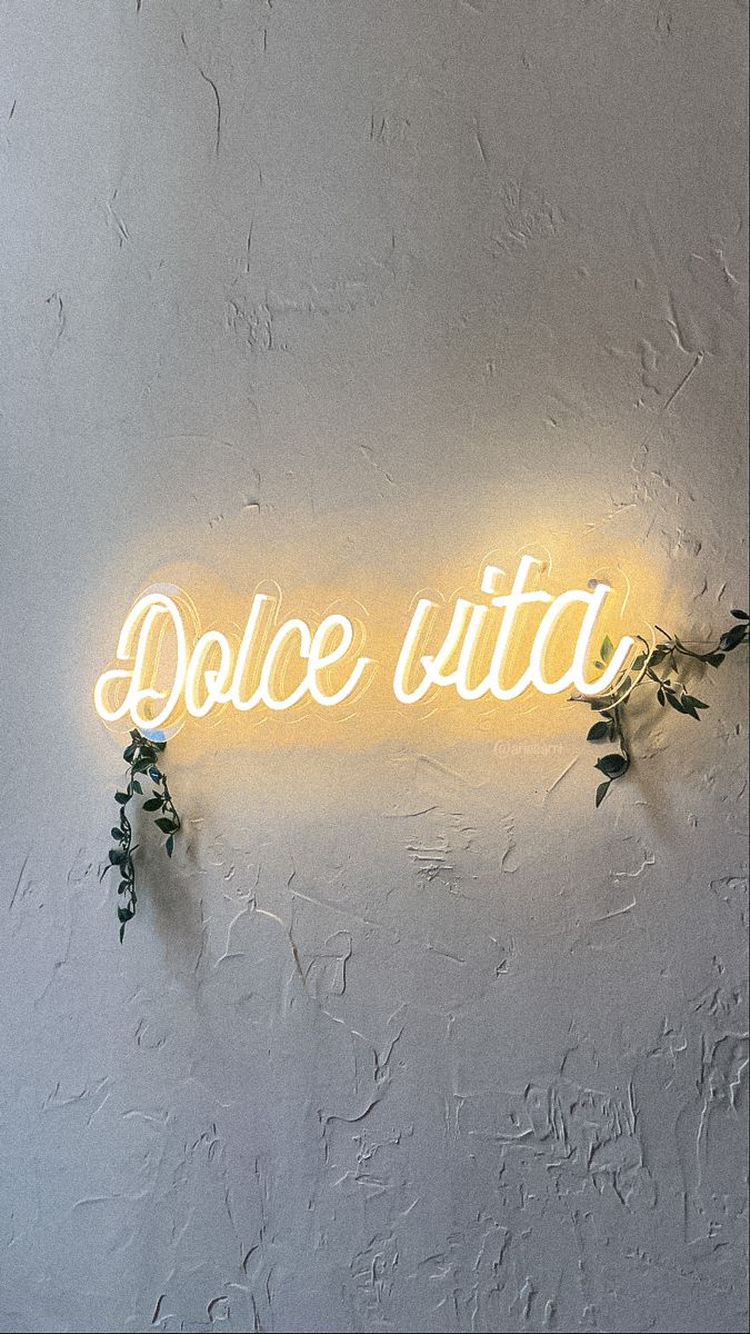 a neon sign that says dolce vita on the side of a wall with flowers