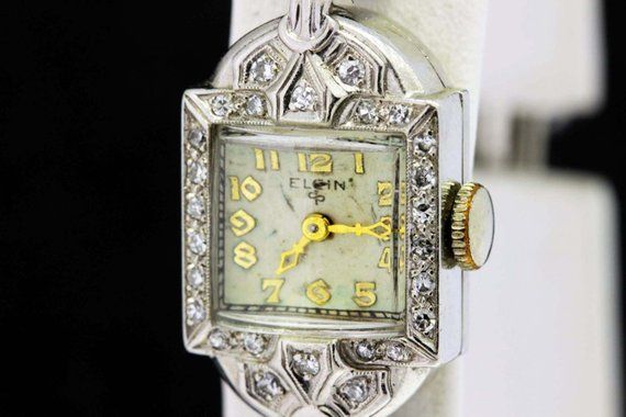 This Elgin wrist watch is made in platinum and has pave diamonds on the case of the watch. The crystal is domed, there is engraving, and  also milgrain accents. The diamonds are estimated to be G/H color and the stones are mostly eye-clean. The band is a braided cord with a sliding hing that walks up and down on a fixed section.The watch measures 14.38mm wide, 29.78mm long, and sits 8.77mm tall. The watch weighs about 0.46mm oz.This watch is in working condition and comes with a 1 year guarantee Anniversary Diamond Watch With Pave Setting, Diamond White Diamond Watch With Rhinestones For Formal Occasions, Diamond White Watch With Rhinestones For Formal Occasions, White Gold Diamond Watch With Rhinestones, Formal Diamond White Watch With Rhinestones, Art Deco Diamond Watches With Diamond Accents, Evening Diamond Watch With Art Deco Style, Evening Art Deco Diamond Watch With Accents, Elegant Single Cut Diamond Jewelry For Wedding