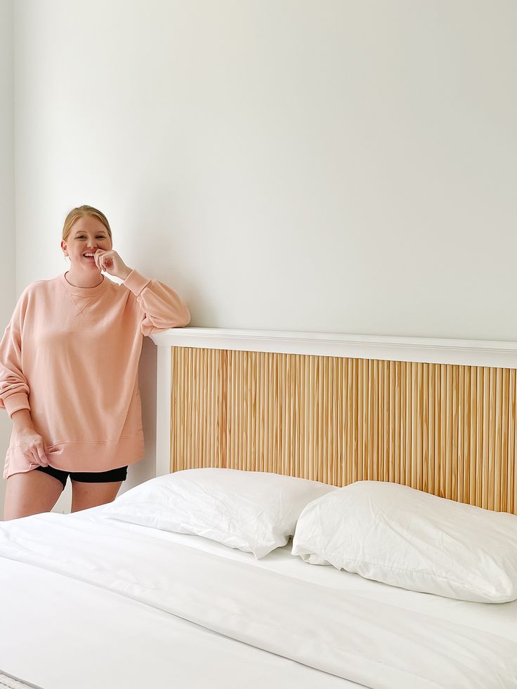 a woman standing next to a bed with white sheets