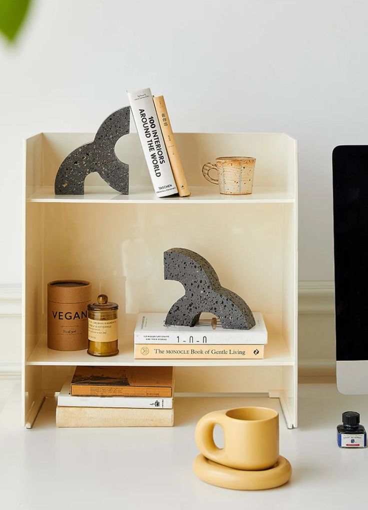 a desk with a computer, coffee cup and other items on the shelf next to it