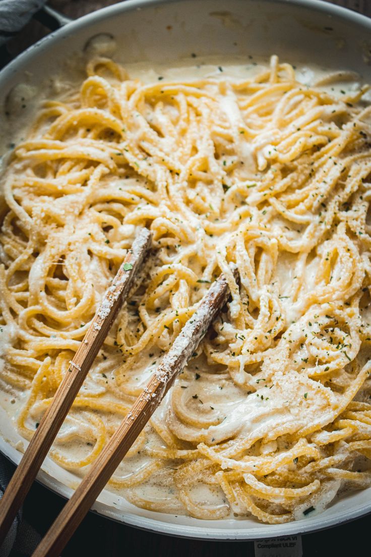 two wooden chopsticks in a bowl of pasta with sauce and parmesan cheese