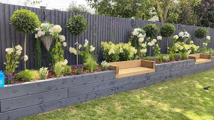 an outdoor garden with flowers and plants growing on the side of a fenced in area