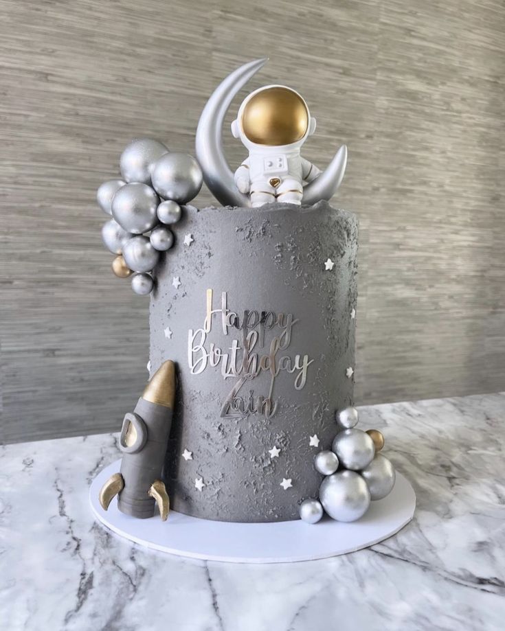 a birthday cake decorated with silver and gold decorations on a marble countertop next to a rocket ship