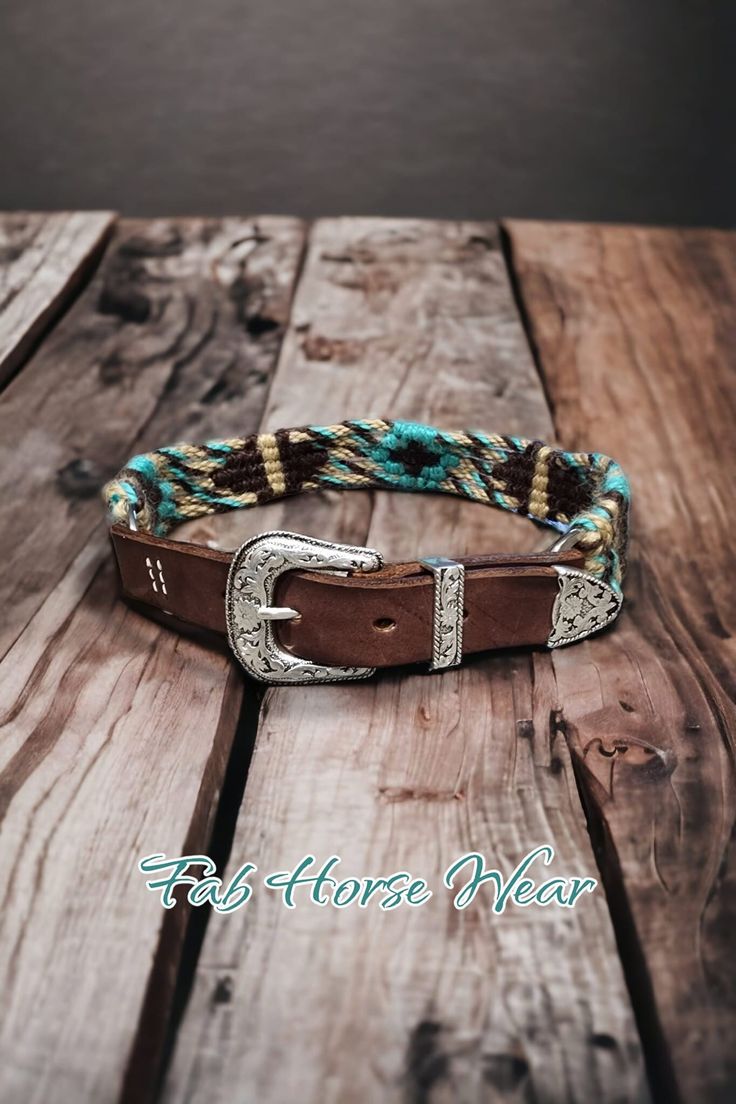 a brown leather belt with turquoise and gold braiding on top of wooden planks