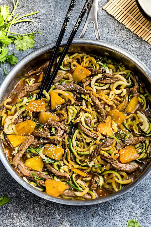 a pan filled with noodles and meat on top of a table next to chopsticks