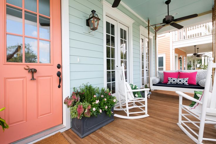 a porch with rocking chairs and potted plants on the front porch next to an orange door